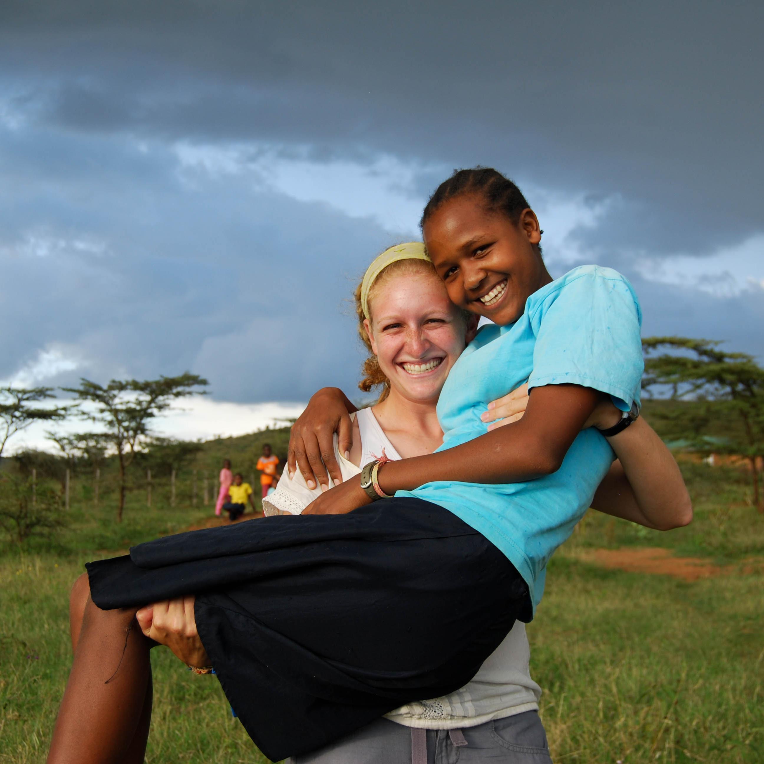 Two smiling people outside at Daraja Academy with a scenic background.