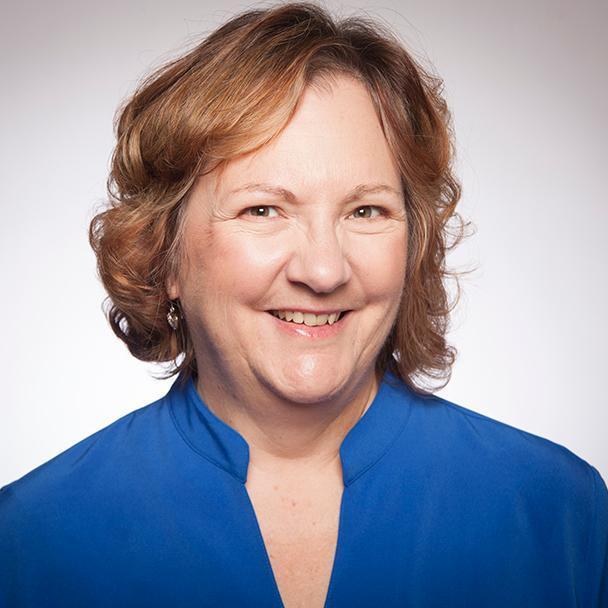 Woman wearing a blue blouse, smiling against a plain background.