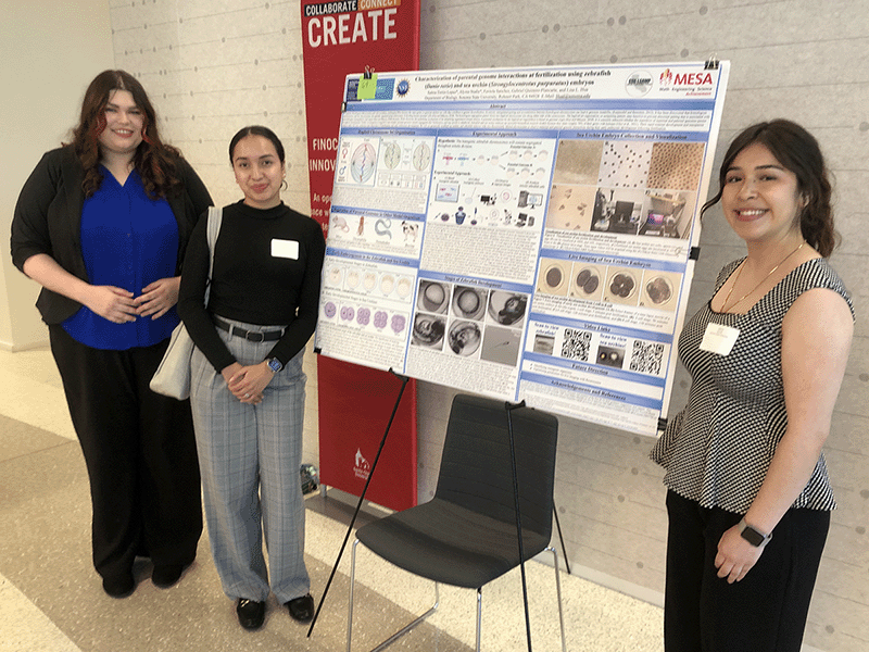 Three students stand next to their poster