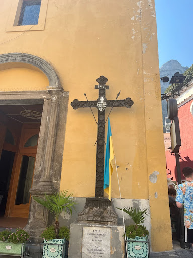 Cross on pedestal in front of a yellow building facade.