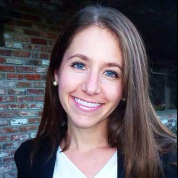 A person smiling in front of a brick wall.