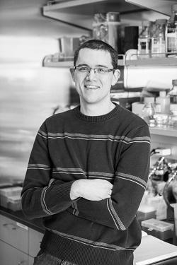 A person in a kitchen, wearing glasses and a dark sweater.