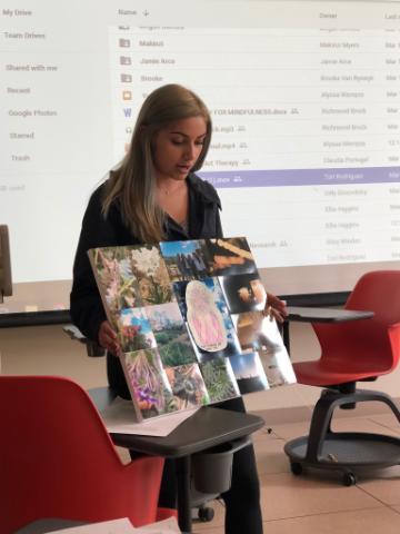 A woman presenting a collage in a classroom setting.