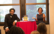 Two people sitting at a red-draped table, speaking to an audience.