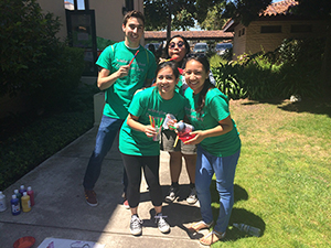 Group of people in green shirts posing with trophies in a garden.