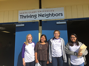 Four smiling students standing in front of a building with 