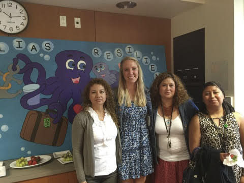 Four people are standing in front of a decorated bulletin board.