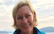 A smiling person with mountains and sky in the background.