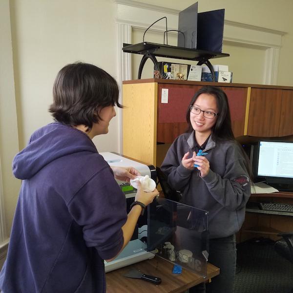 Alt text: Two people operating a 3D printer in an office setting.