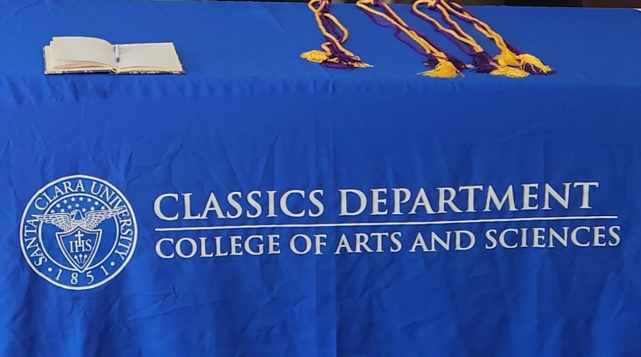 12 students behind a table with a royal blue tablecloth wearing purple and gold honor cords as 2023 Eta Sigma Phi inductees