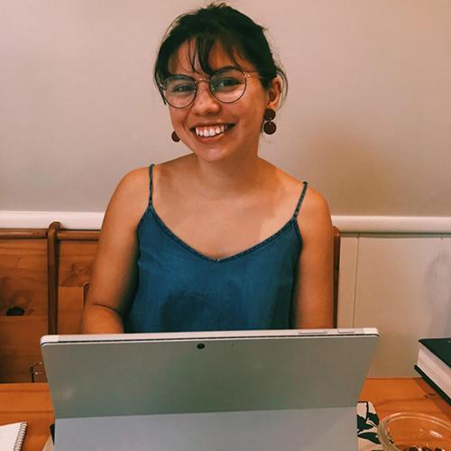 A person smiles while working on a laptop at a table.