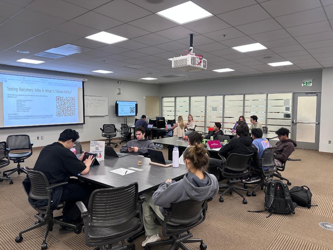 SCU students in a media room with a screen showing a powerpount slide with a QR code