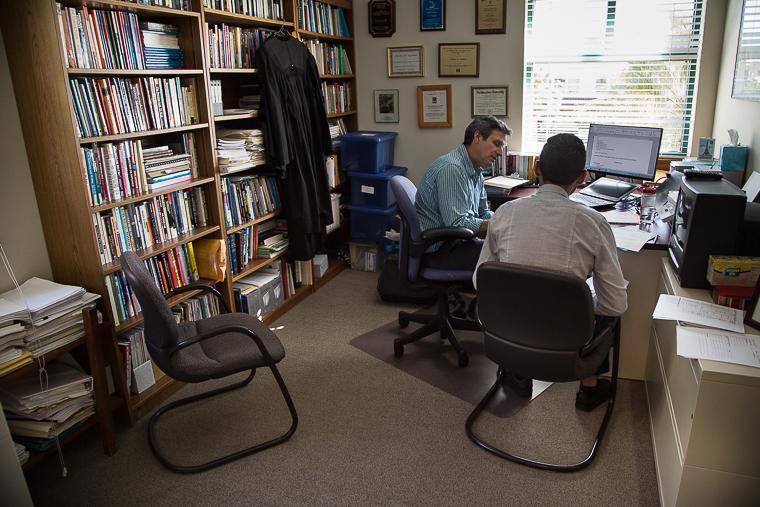 Two people working on computers in a cluttered home office.