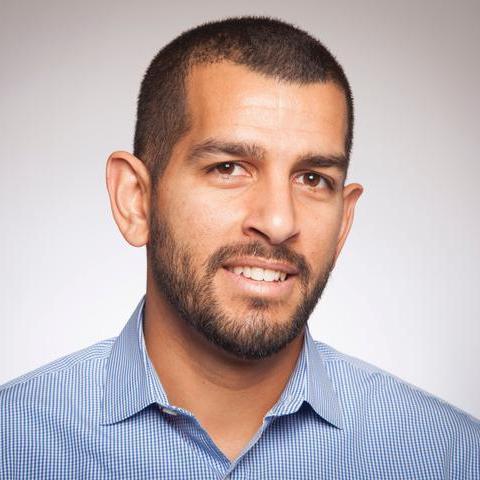 Alt text: Andrew Ishak, smiling, wears a light blue shirt against a neutral background.