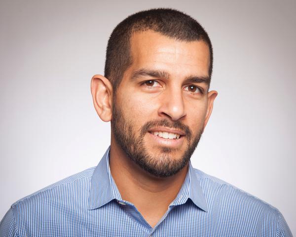 Alt text: Andrew Ishak, smiling, wears a light blue shirt against a neutral background.