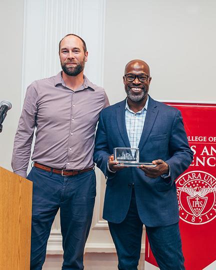 Kafui Dzirasa holding his speaker's plaque next to Brian Bayless at a recognition dinner 