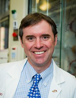 A man wearing a white lab coat and blue tie.