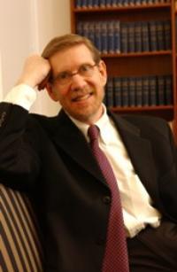 A person seated, smiling, with bookshelves in the background.