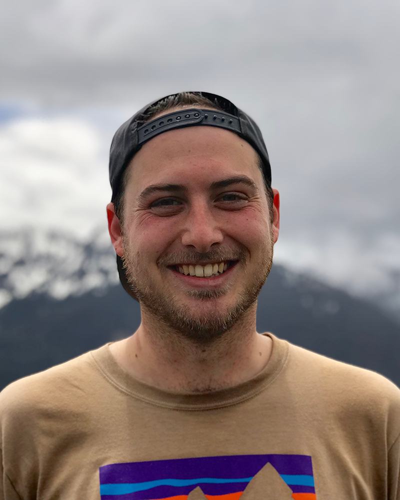 Zach Milkis headshot with mountains and dark clouds in he background