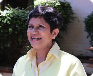 A person smiling outdoors with greenery in the background.