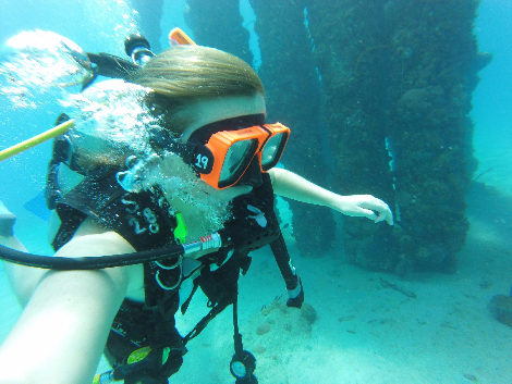 Person scuba diving underwater near large structures.