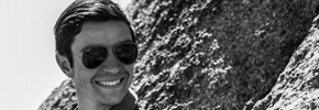 Smiling person with sunglasses in front of a rock formation.