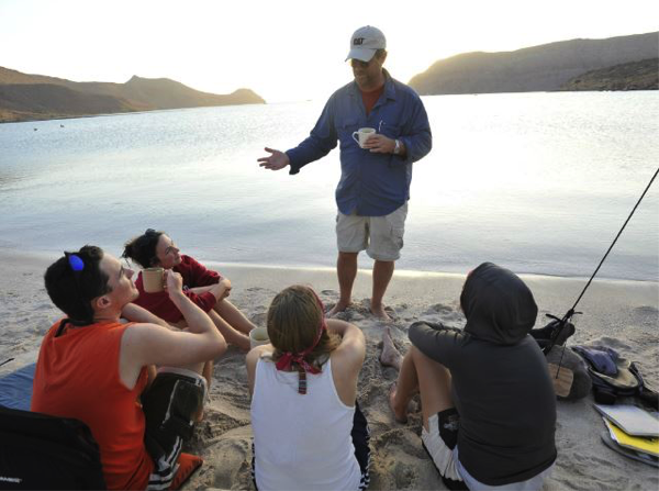 A person standing and talking to a group by the water.