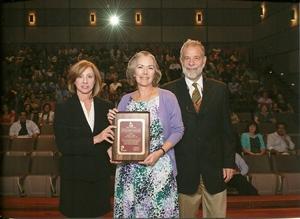 Three people holding an award on a stage during a ceremony.