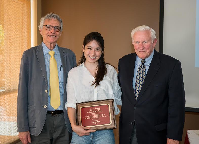 Three people standing; person in the middle holds a framed plaque.