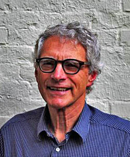 A man with glasses against a brick wall background.