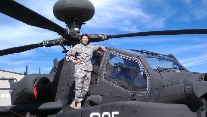 A person in military uniform standing beside a helicopter.