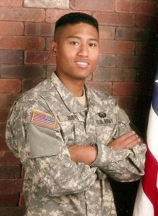 A person in a military uniform stands next to the American flag.