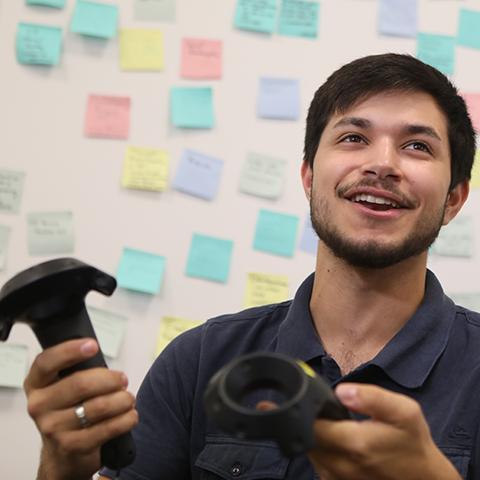 A person holding VR controllers with sticky notes in the background.