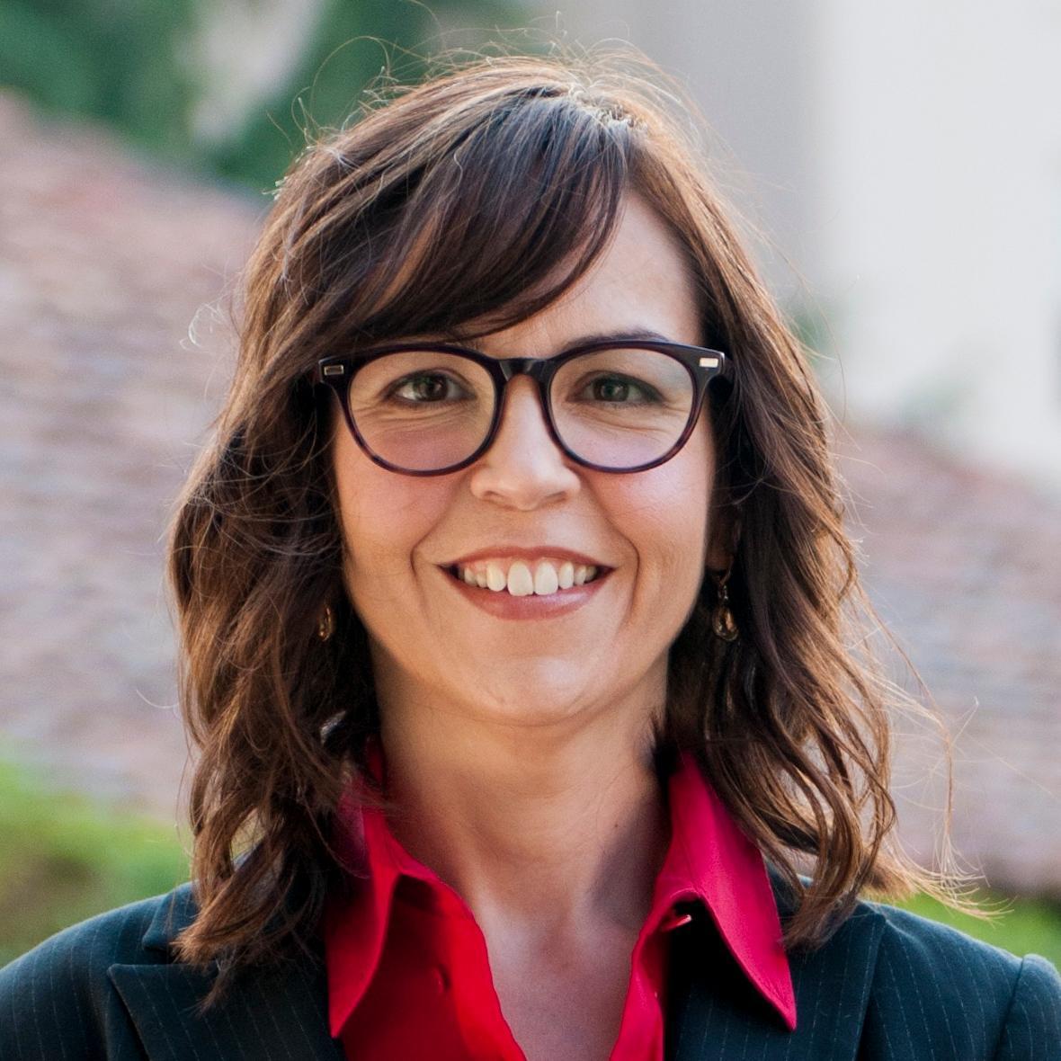 A person wearing glasses, a red shirt, and a black blazer.