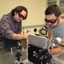 Two people working with scientific equipment, wearing protective eyewear in a laboratory setting.