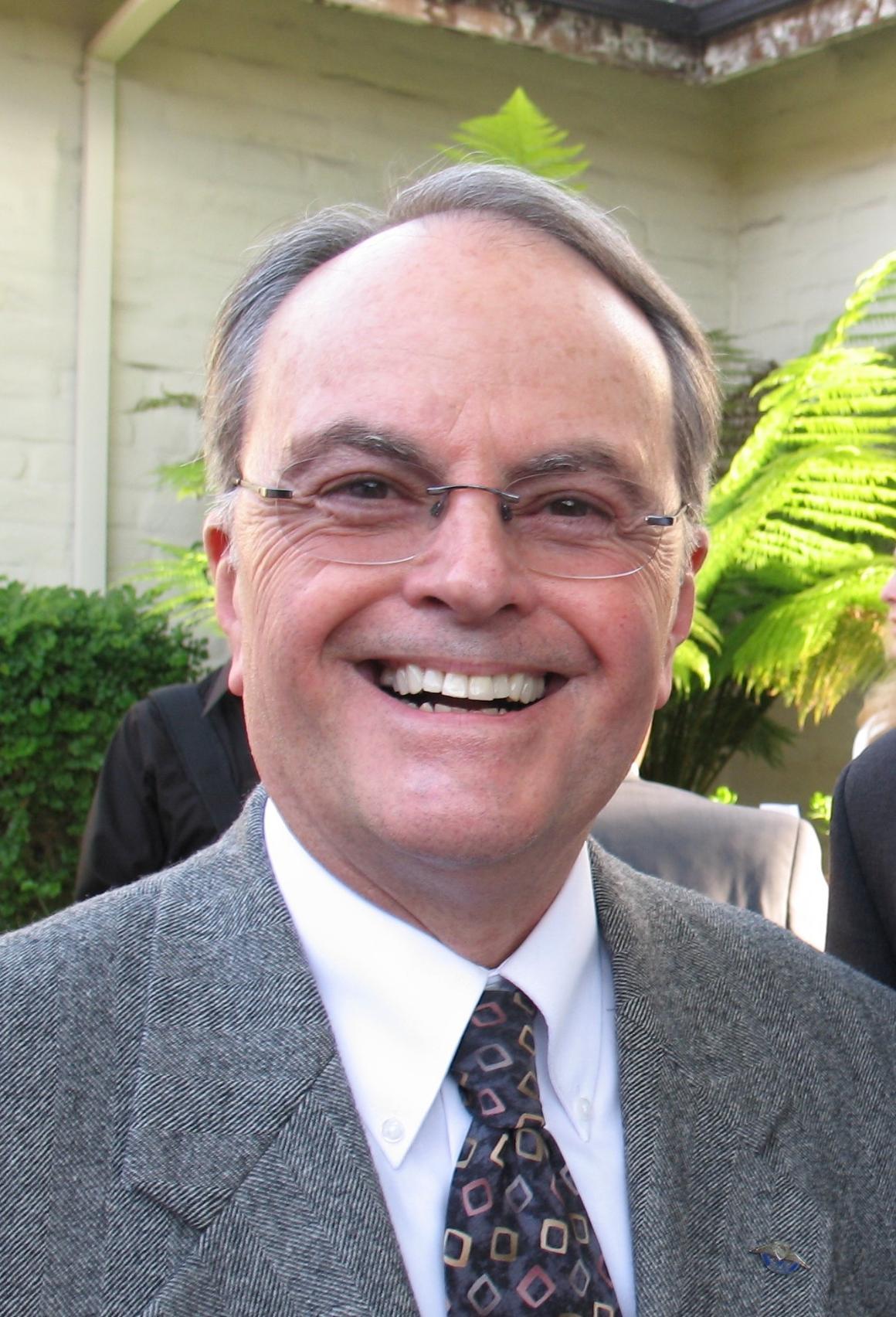 A man in a suit and tie smiling outdoors.