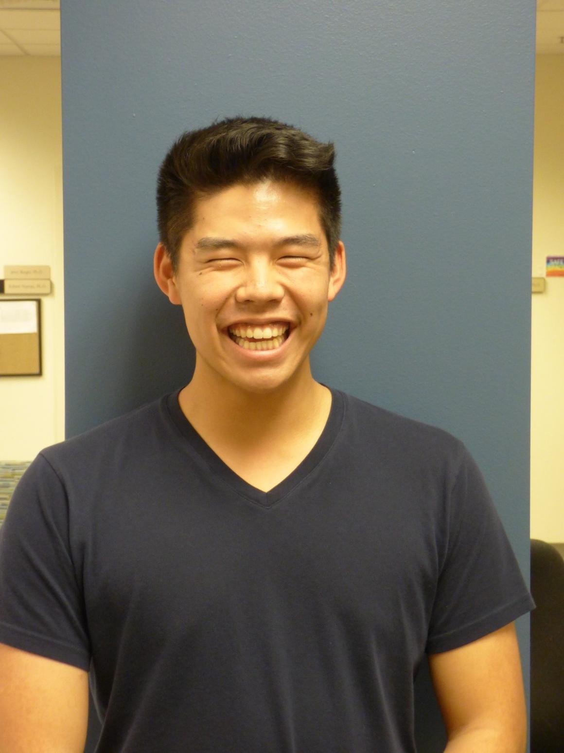 A person smiling in a dark shirt against a blue background.