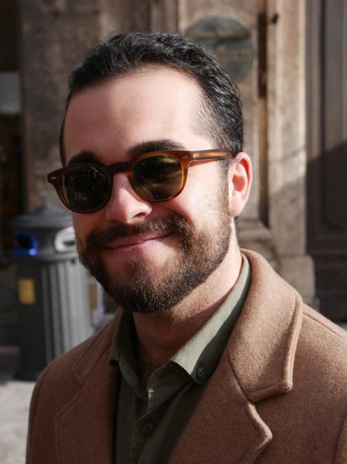 A person wearing sunglasses and a coat smiling outdoors.