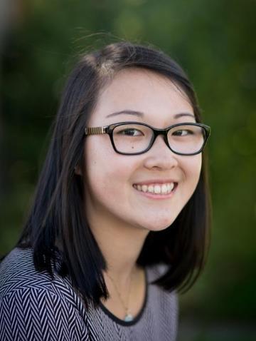 A person smiling, wearing glasses, against a blurred green background.