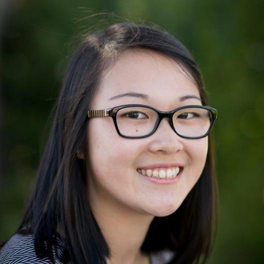 A person smiling, wearing glasses, against a blurred green background.