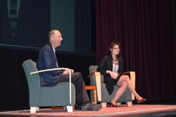 Two people seated on stage at a speaking event.