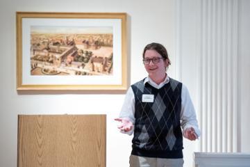 Person standing in front of a framed artwork, engaging in discussion or presentation.