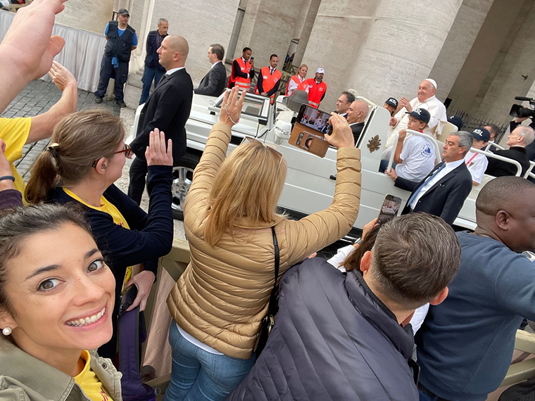 Elyse Raby selfie with crowd and Pope Francis going by in the popemobile in the distance.