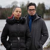 Two people standing outdoors in winter clothing near a body of water.