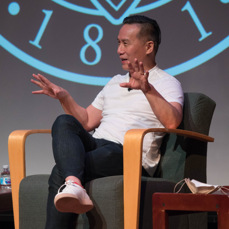 Person talking while seated in an armchair on a stage.