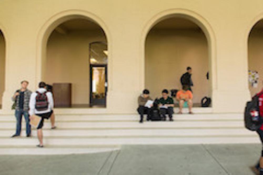 People gathered around arched doorways outdoors, some seated on steps and others walking.