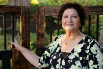 A woman standing outdoors, holding a railing, smiling at the camera.