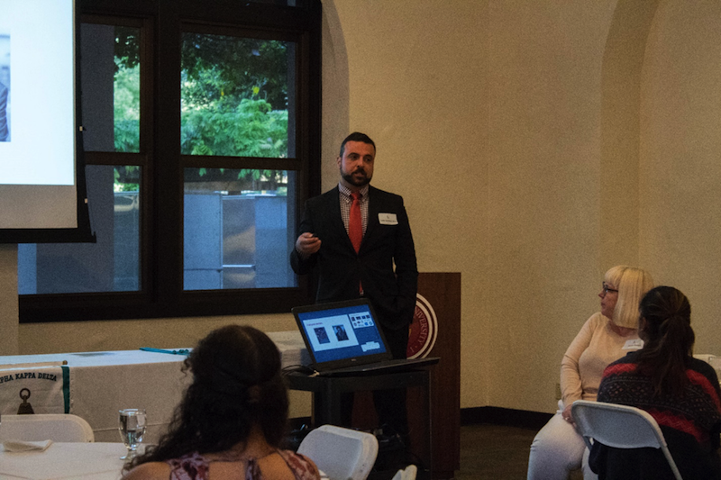 A person presenting at a seminar with people seated and a laptop.