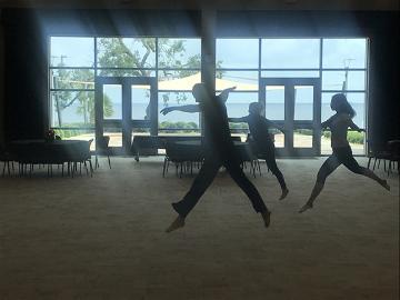 Three people leaping in front of large windows in a gym.