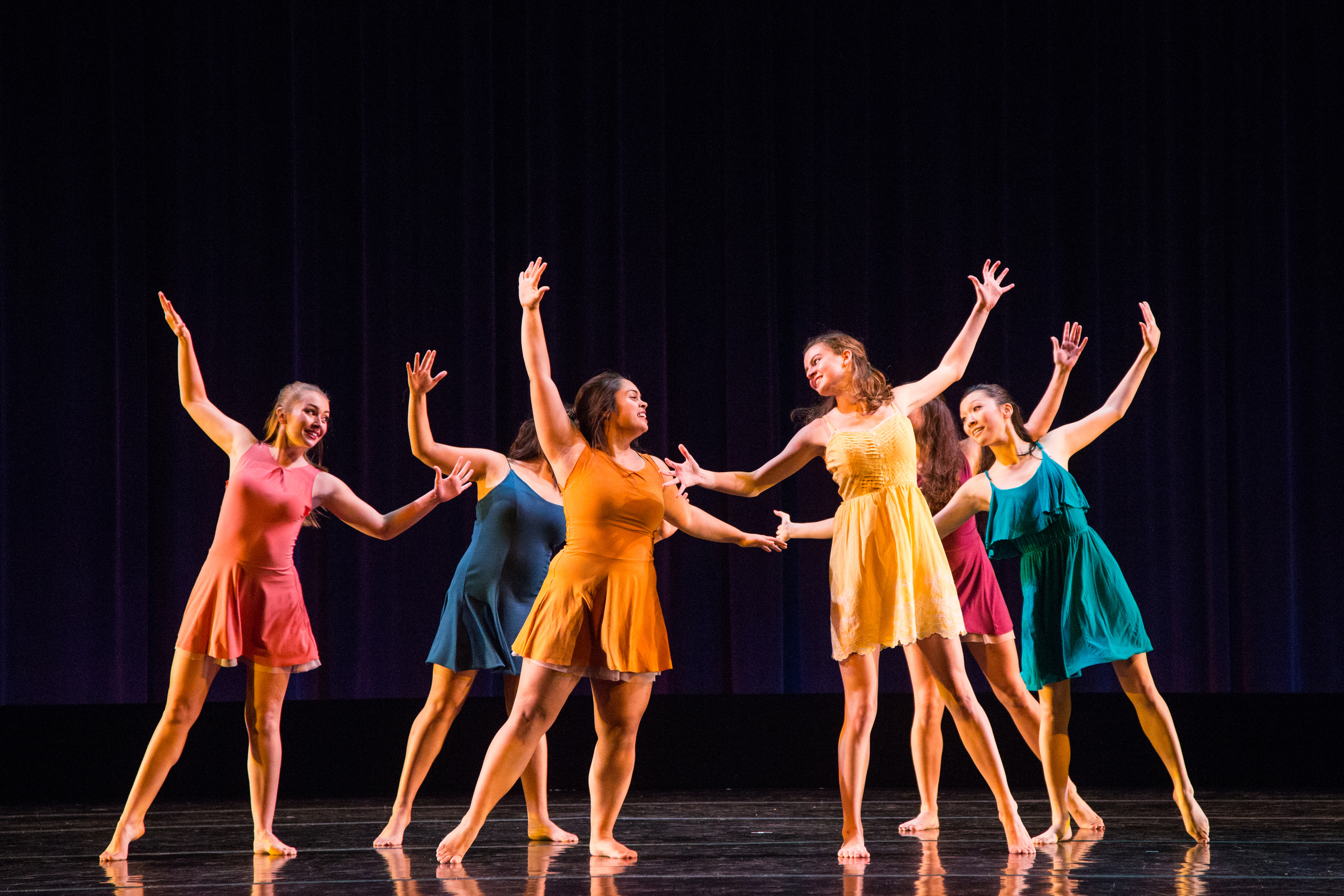 Six dancers performing choreography on stage wearing brightly colored costumes.